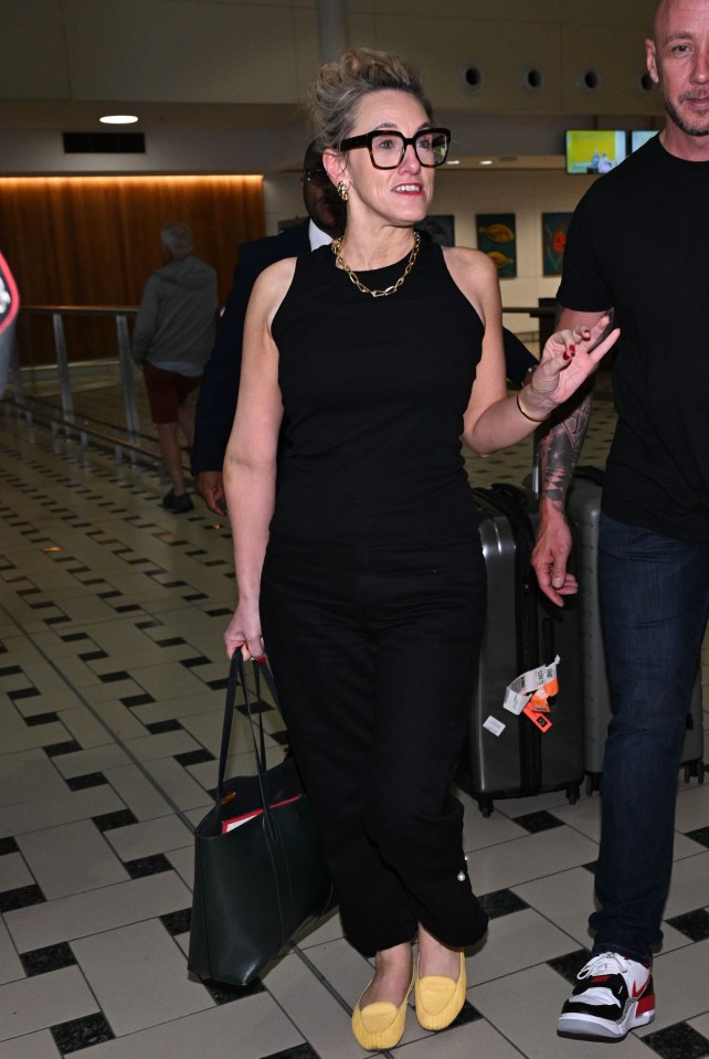 a woman wearing glasses and a black top is walking through an airport