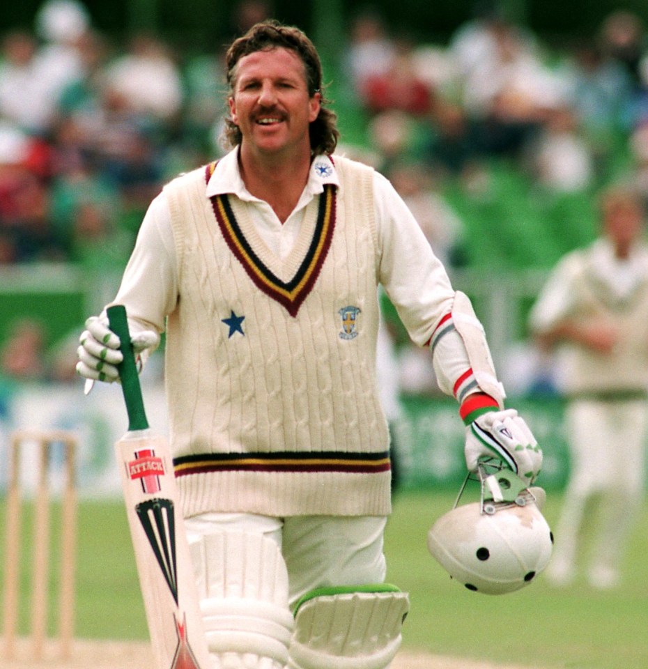 a man in a white sweater with a star on it is holding a cricket bat