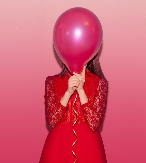 a woman in a red dress holds a pink balloon in front of her face