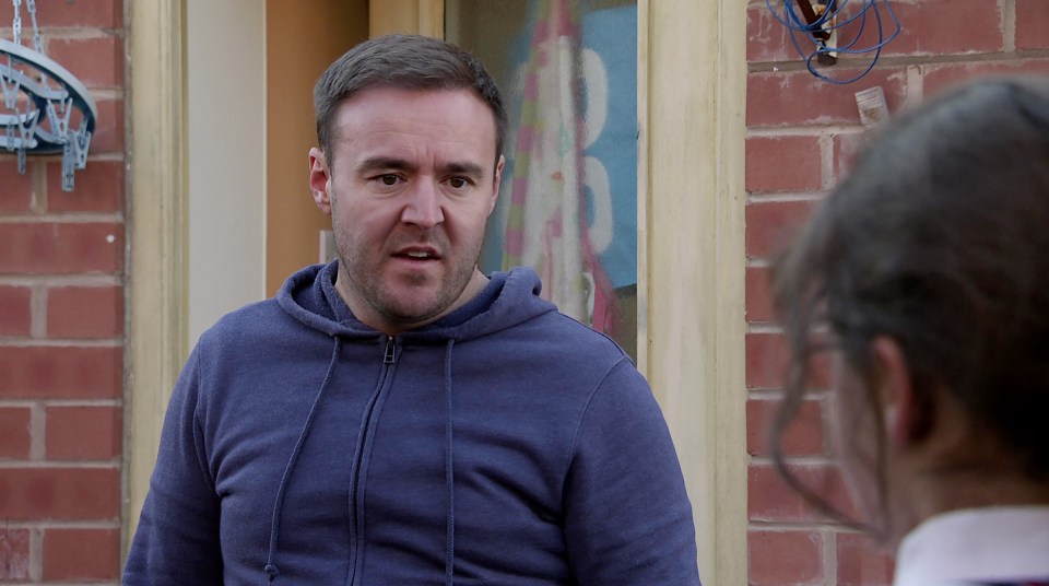 a man in a blue hoodie is talking to a girl in front of a brick wall