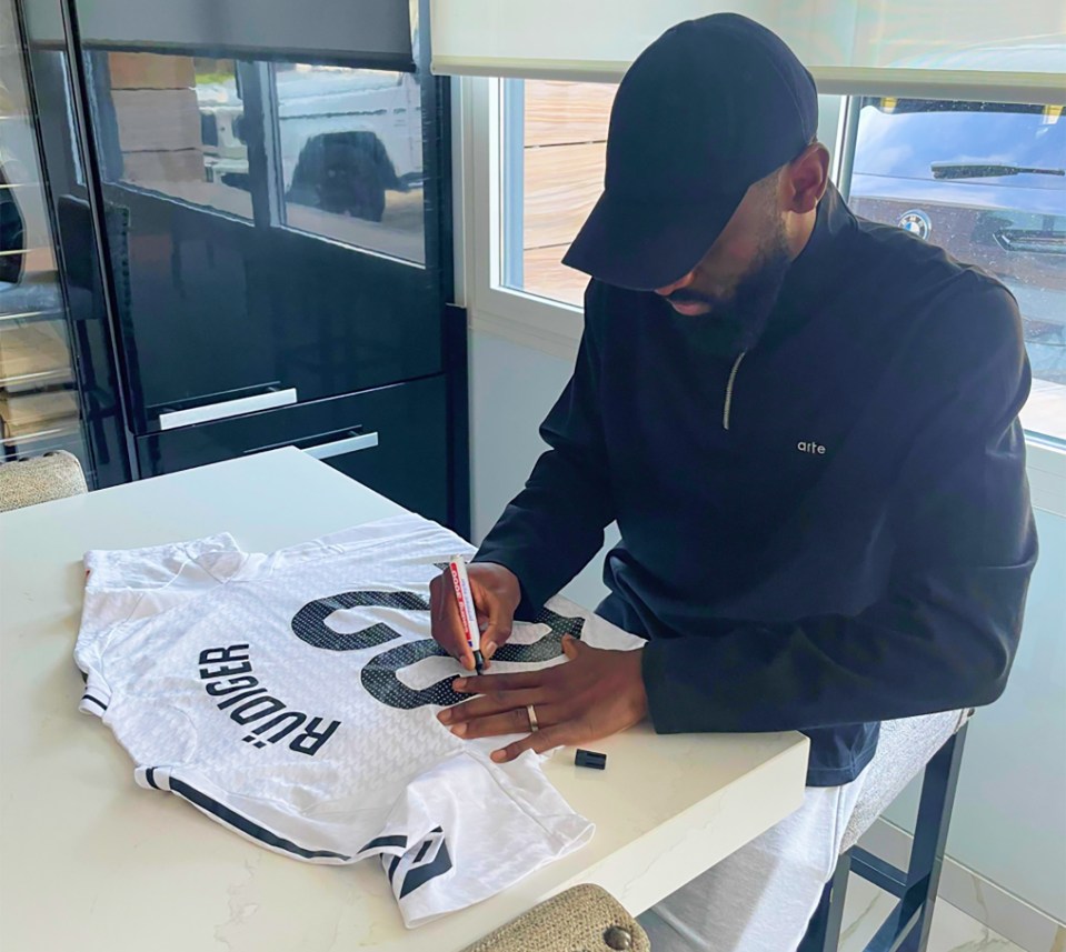 a man sitting at a table signing a jersey with the name rudiger on it