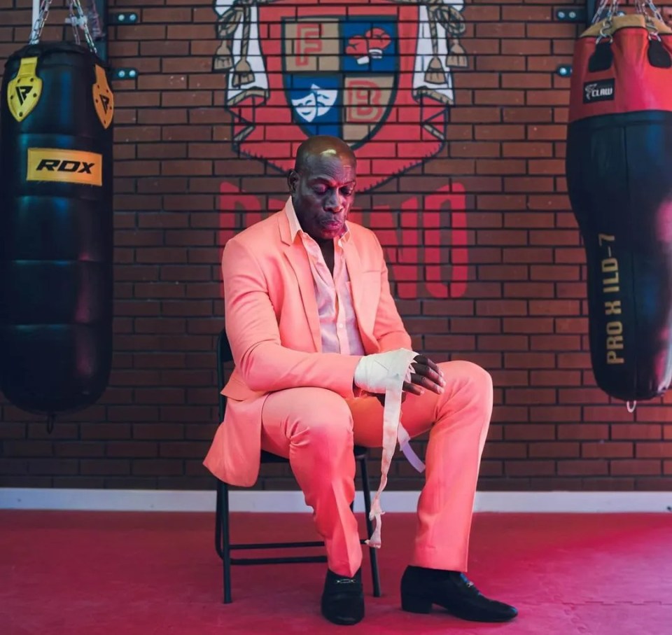 a man in a pink suit sits in front of a boxing bag that says rox