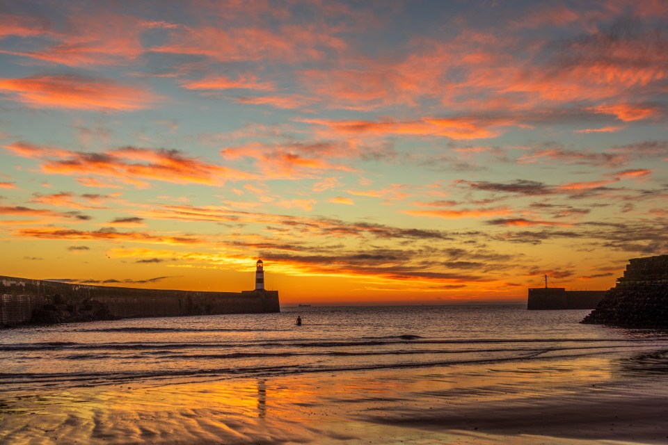 a sunset with a lighthouse in the distance