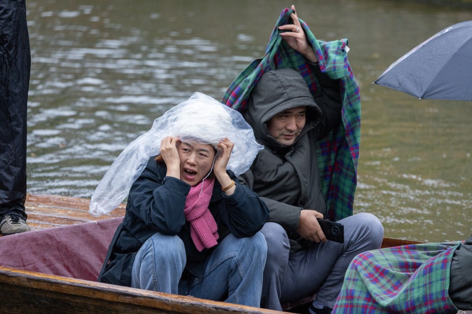 People trying to shelter from the rain as they go for a punt on the River Cam in Cambridge