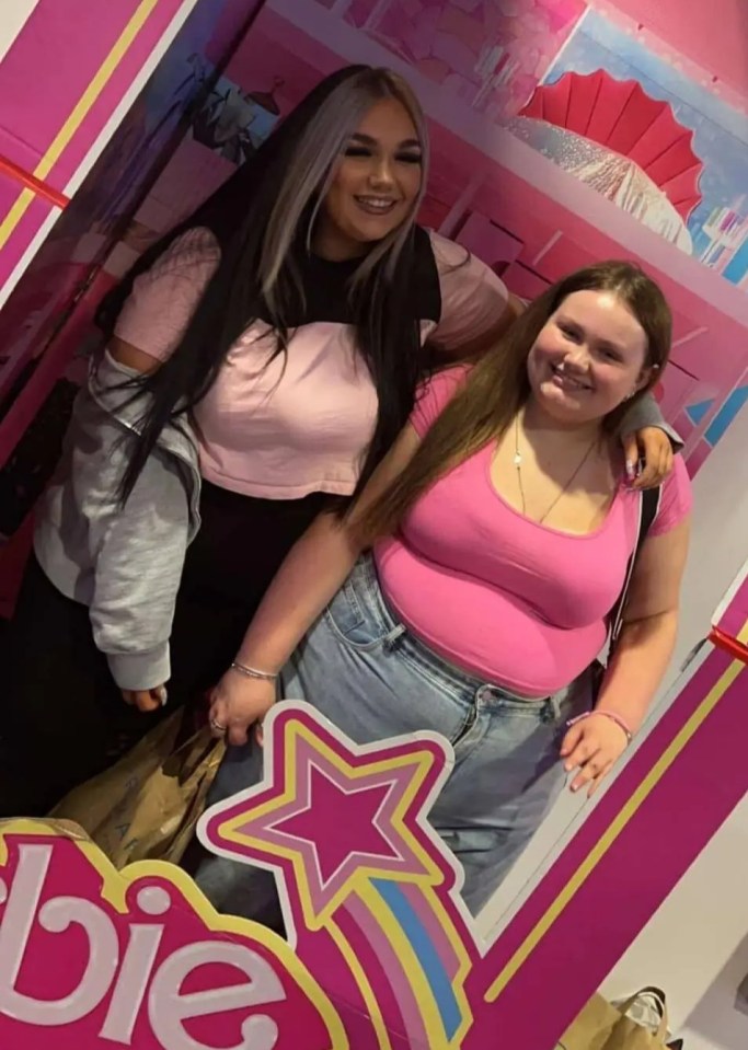 two girls pose in front of a barbie doll box