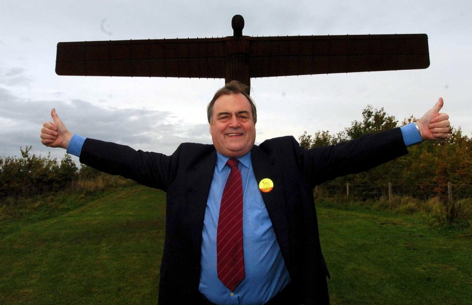 a man in a suit and tie is giving a thumbs up in front of an angel of the north statue