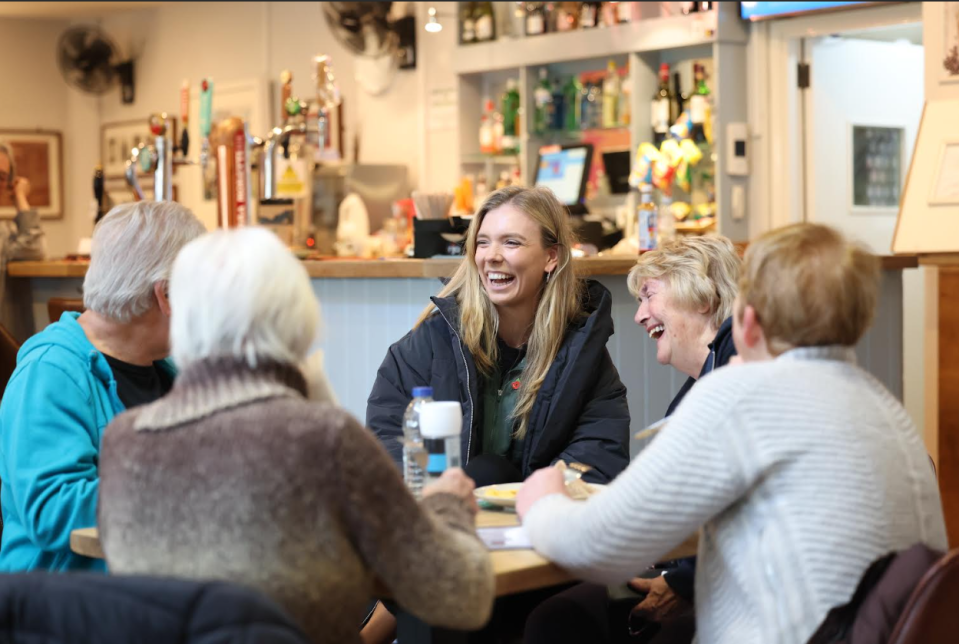 a woman laughs while sitting at a table with other people