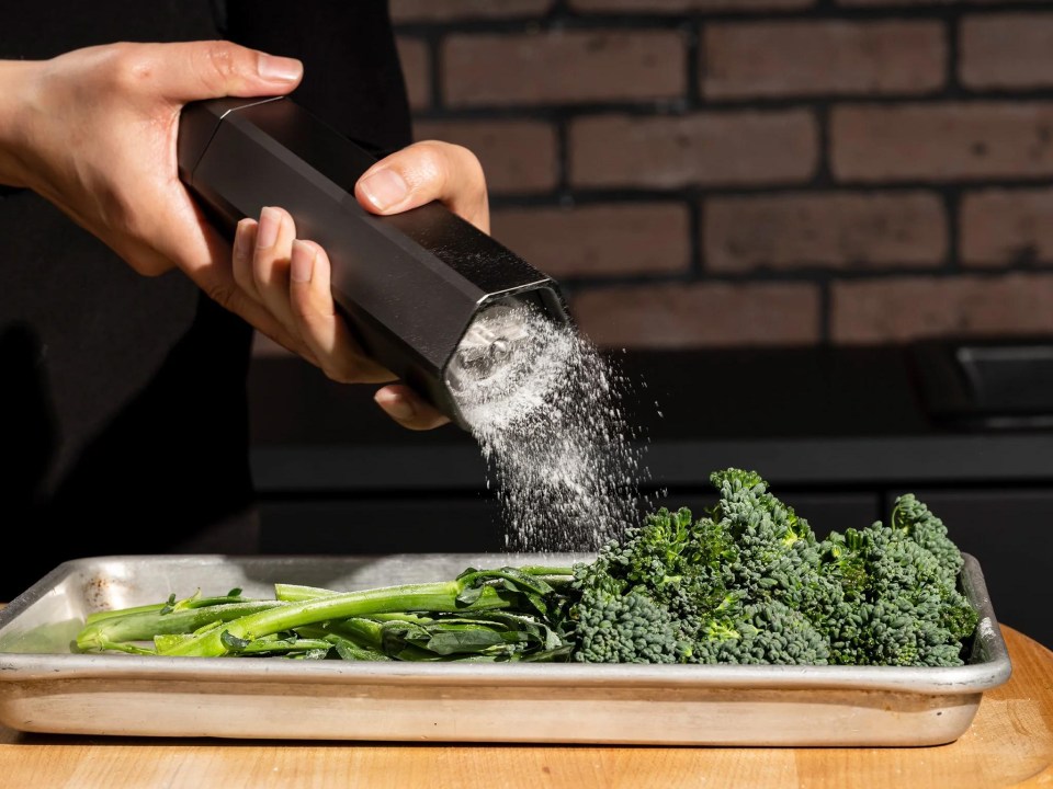 Salt being sprinkled on broccoli in a metal pan.