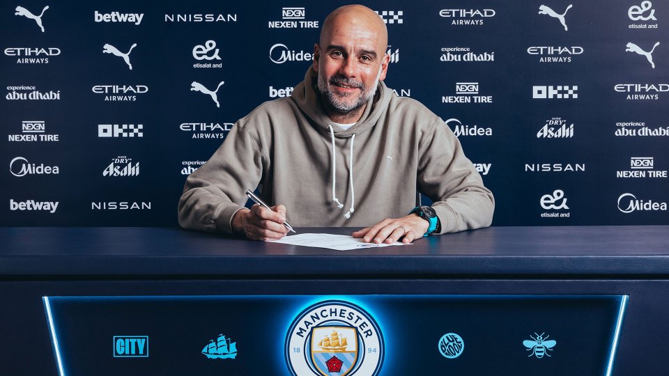 a man signing a document in front of a manchester city sign