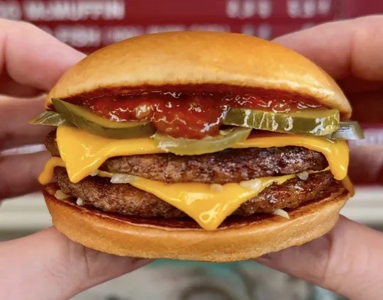 a person is holding a double cheeseburger with pickles and ketchup .