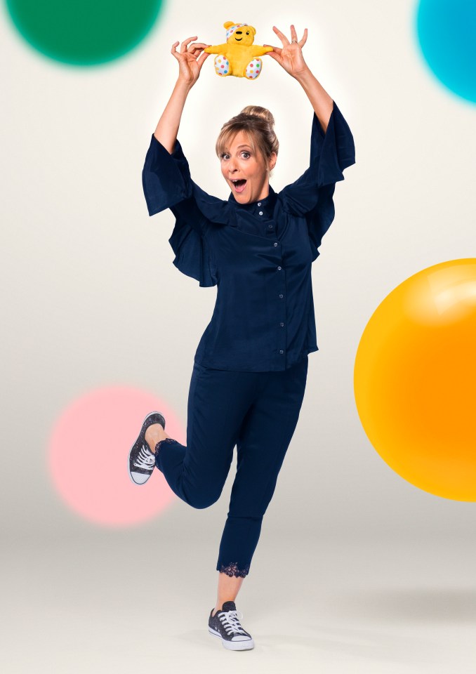 a woman in a blue shirt is holding a yellow teddy bear over her head