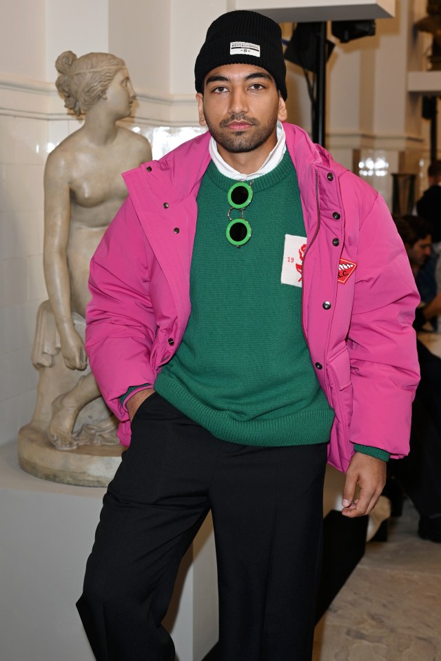 a man wearing a pink jacket and a green sweater stands in front of a statue