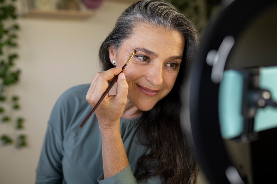 a woman brushes her eyebrows in front of a mirror