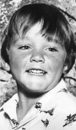 a black and white photo of a young boy smiling for the camera .