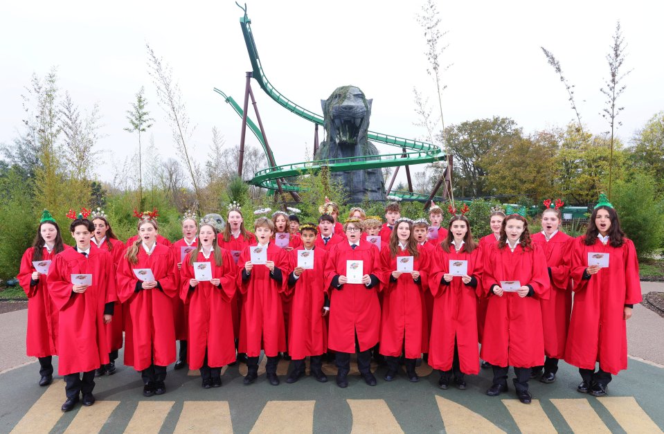 A group of people in red gowns are singing in front of a roller coaster