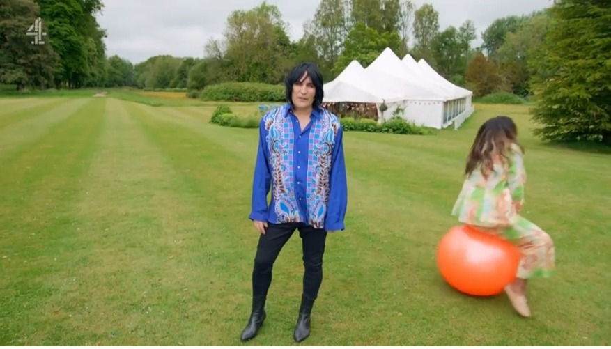 a man in a blue shirt is standing in a grassy field next to a woman on a bouncy ball