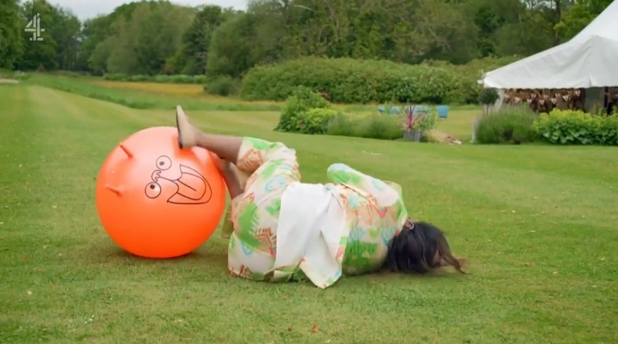 a woman is laying on the grass next to an orange ball with a face on it