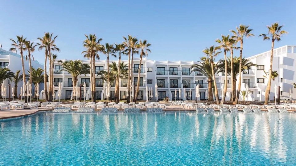 a large swimming pool in front of a hotel with palm trees