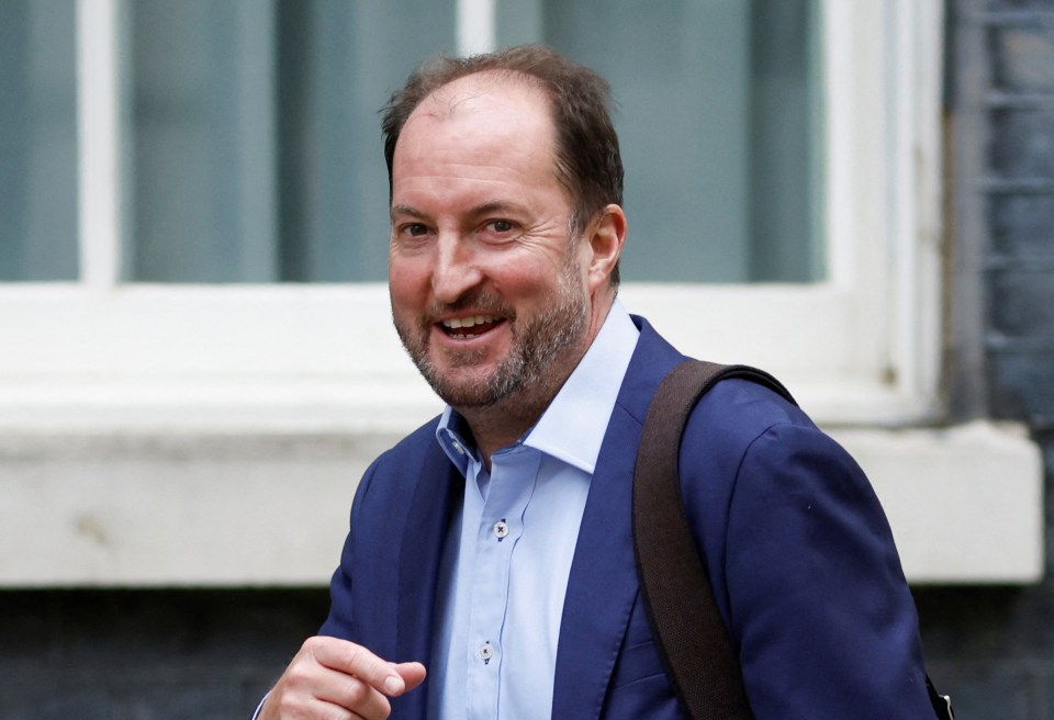 a man wearing a blue suit and carrying a brown bag is smiling and pointing