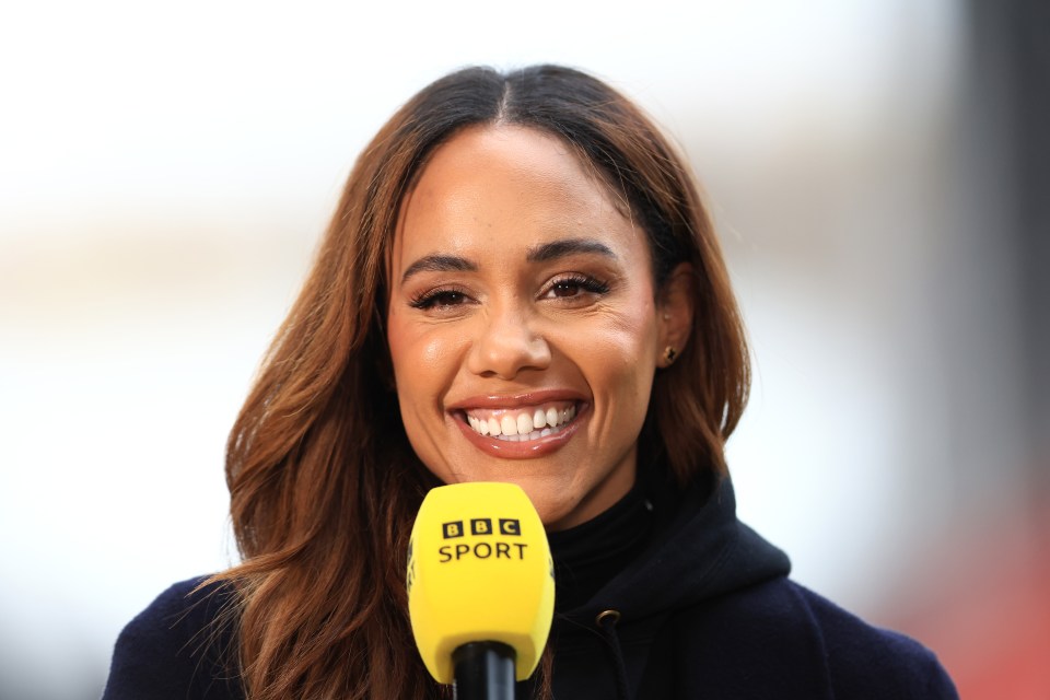 a woman is smiling while holding a yellow bbc sport microphone