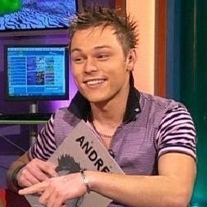 a young man in a striped shirt is holding a book and pointing at it .