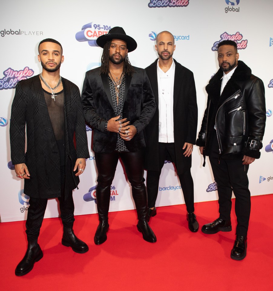 four men standing on a red carpet in front of a sign that says jingle bell