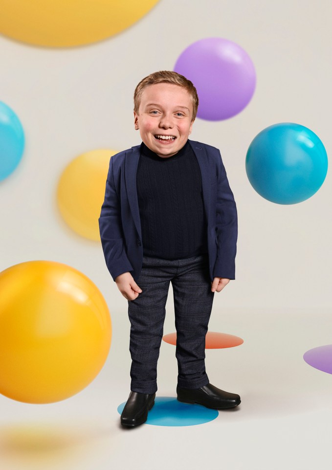 a young boy in a suit stands in front of balloons