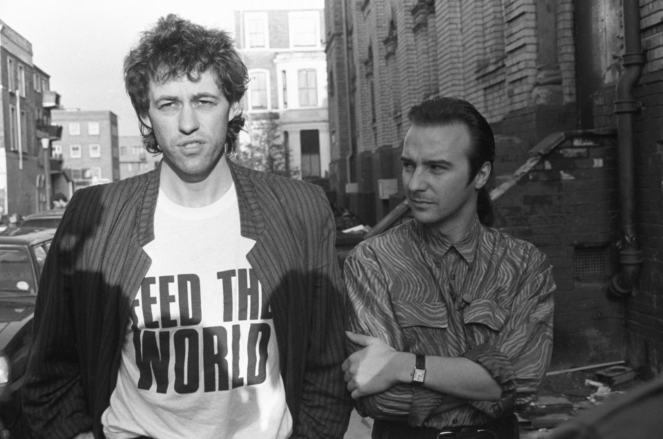 a man wearing a feed the world shirt stands next to another man