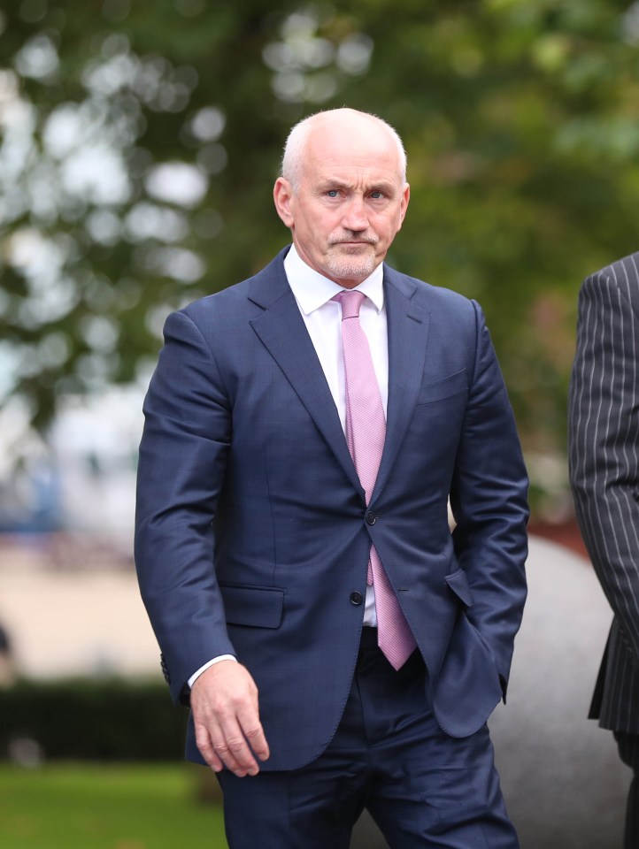 a man in a suit and pink tie stands with his hands in his pockets