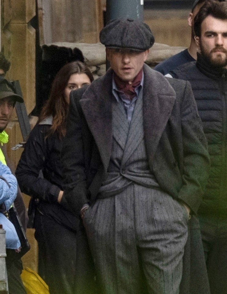 a man wearing a hat and a coat stands in a crowd