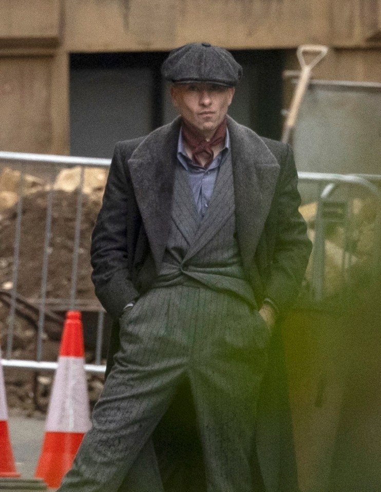 a man in a suit and hat stands in front of a fence