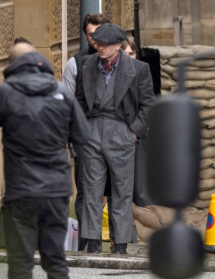 a man in a suit and hat stands in front of a building