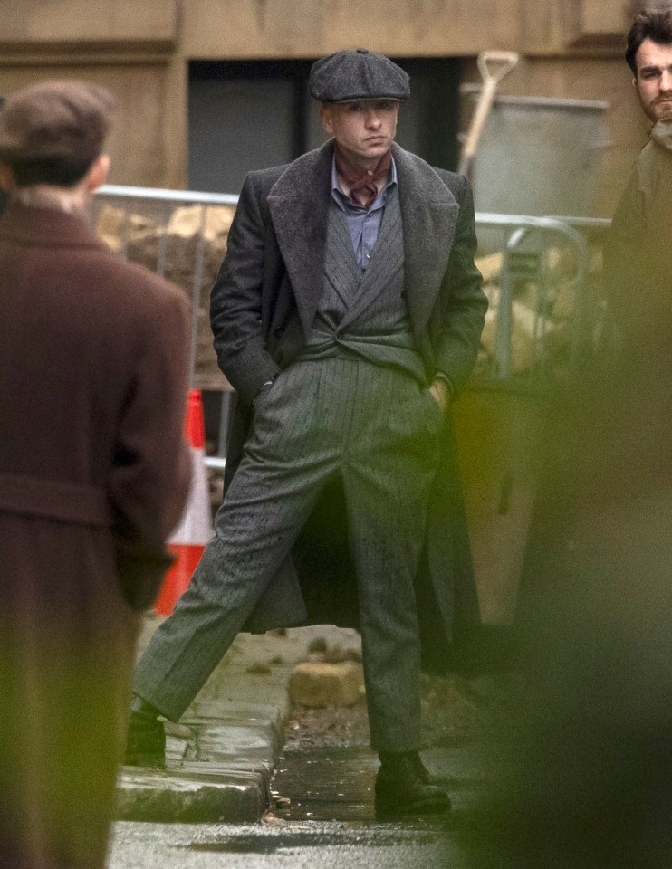 a man in a suit and hat is standing on a sidewalk