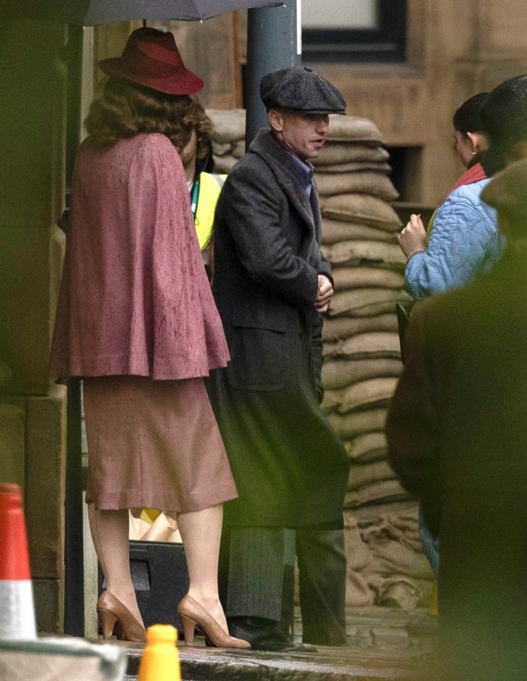 a woman in a pink coat stands next to a man in a hat