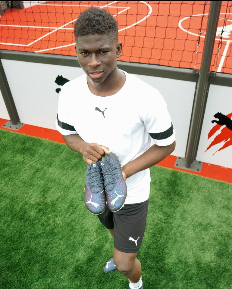 a young man holding a pair of puma soccer cleats