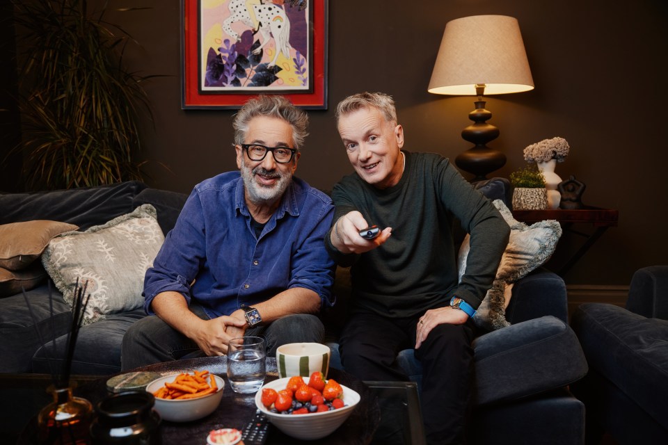 two men are sitting on a couch and one is holding a remote control