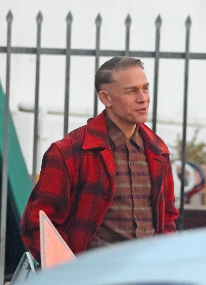 a man in a red plaid jacket stands in front of a fence