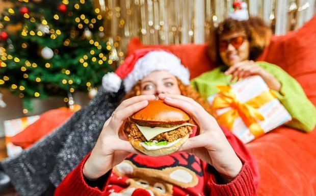 a woman in a santa hat is eating a chicken sandwich