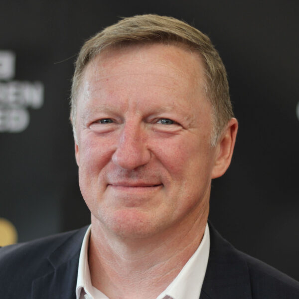 a man in a suit smiles in front of a sign that says screen united