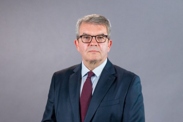 a man in a suit and tie stands with his hands behind his back