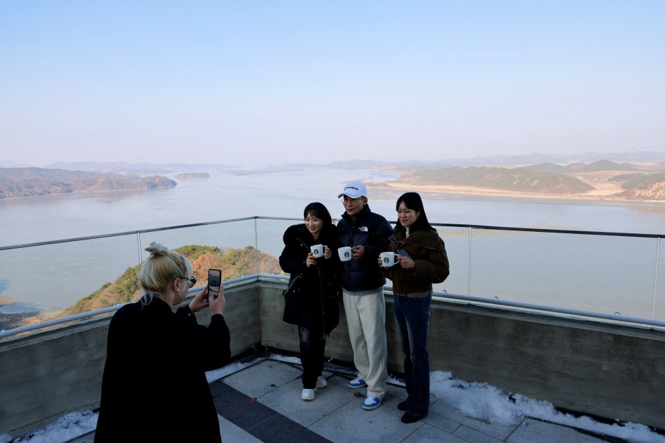 Customers holding a cup of coffee pose to take a picture with North Korea’s propaganda village Kaepoong in the background