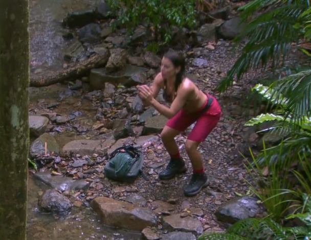 a woman in red shorts squatting next to a river