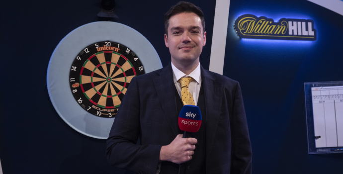 a man holding a microphone in front of a dart board that says unicorn on it