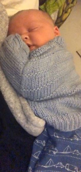 a baby wrapped in a blue sweater is sleeping on a bed .