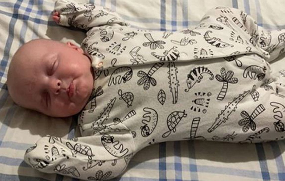 a baby is sleeping on a bed wearing a pajama with animals on it .