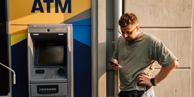 a man stands in front of an atm machine looking at his phone