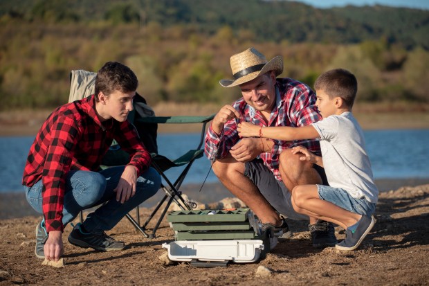 a man in a cowboy hat sits with two boys near a lake