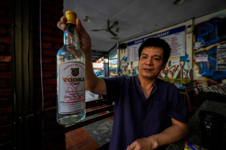 Duong Duc Toan, the manager of Nana Backpack hostel in Vang Vieng, Laos, displays a bottle of Tiger Vodka