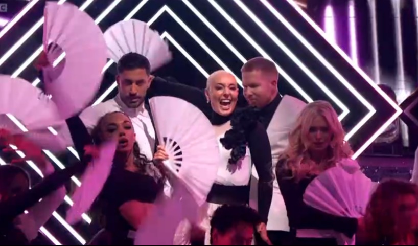 a group of people are dancing with fans on a stage .