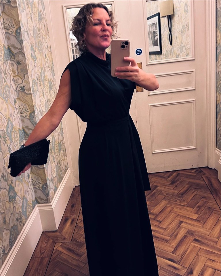 a woman in a black dress is taking a selfie in a hallway